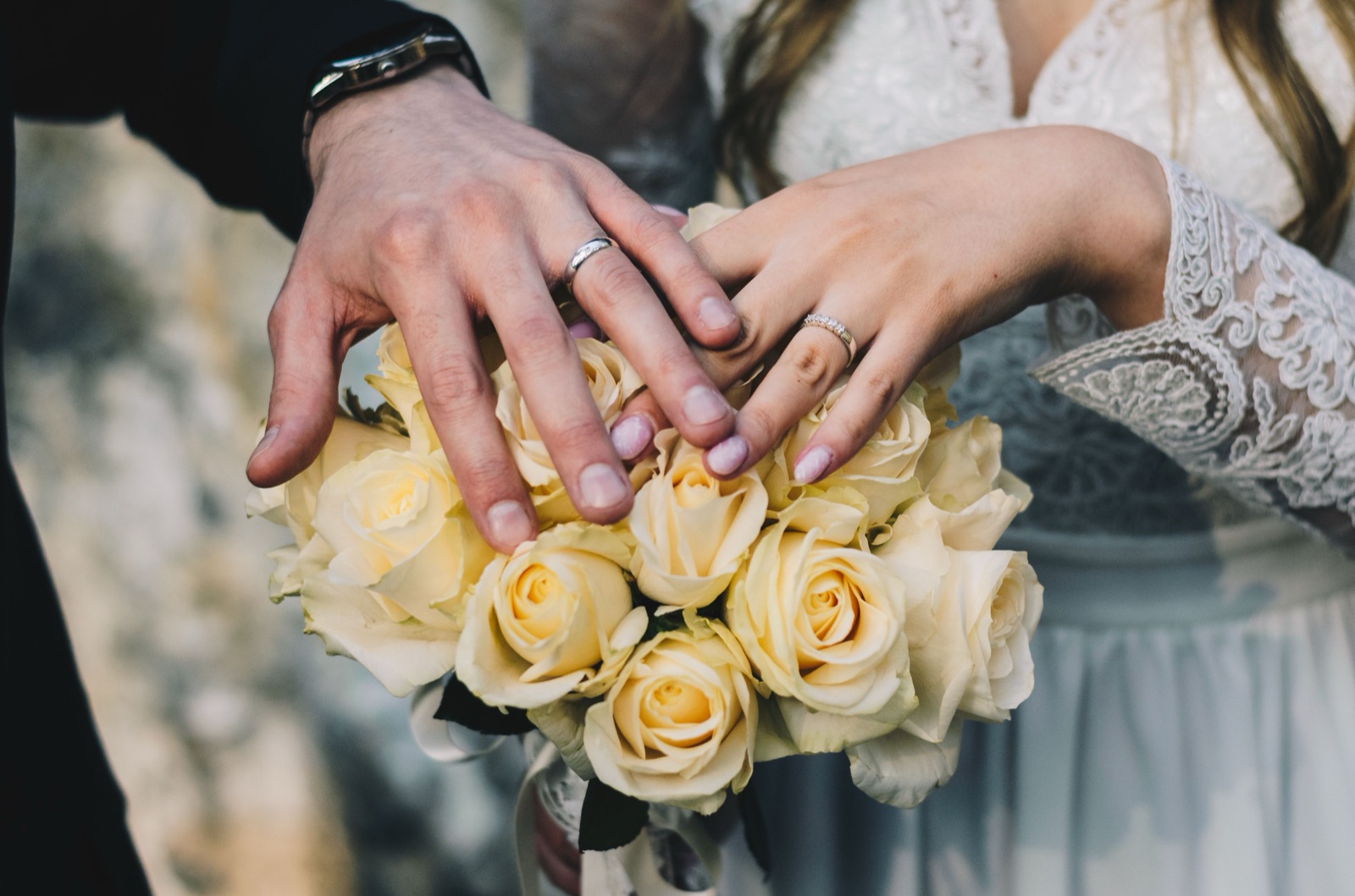 Mains des mariés avec alliances sur un bouquet de roses